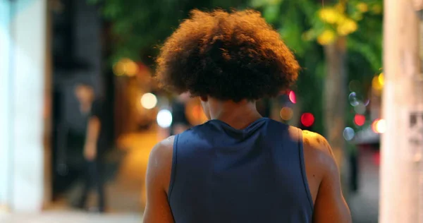 Back of african american black man walking in city sidewalk at night during drizzle