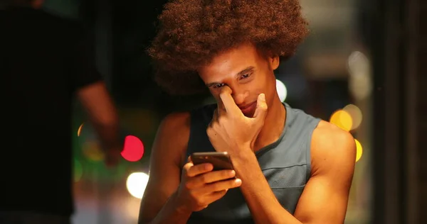 Casual candid african man staring at smartphone in city typing at night