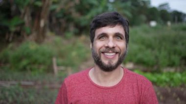 Portrait of a young man walking forward toward camera. Person walks in green agriculture farmland smiling