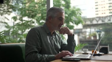 Orta yaşlı bir adam laptopun önünde kahve dükkanında çalışıyor. Yaşlı kişi telefonla mesaj bildirimi alıyor. Bilgisayarda yazan yönetici kişi.