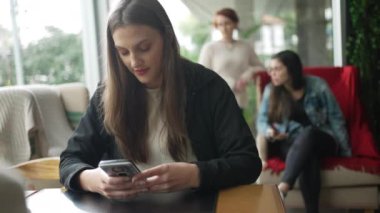 Kahve dükkanında telefon kullanan genç bir kadın. Kafe restoranındaki akıllı telefondan mesaj okuyan kız