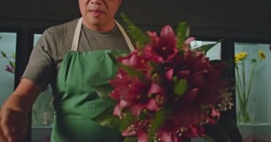 An Asian American florist preparing bouquet of flowers for online delivery. Portrait of an artisan male florist creating artistic arrangement for client at flower shop