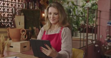Businesswoman owner of flower store holding tablet managing online orders. Portrait of a middle aged small business shop owner inspecting inventory