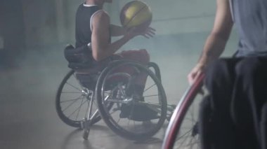 Basketbol oynayan iki engelli sporcu. Tekerlekli sandalyedeki engelli atlet topu takım arkadaşına paslıyor.