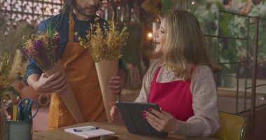 Male employee bringing two bouquet options for female entrepreneur to choose from for client. Small local business concept managing online orders for customers