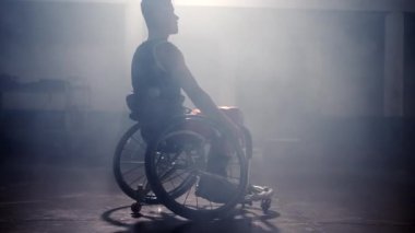 Tekerlekli sandalyedeki engelli atletik adam ve dramatik arka plan ışığı. Hareket kabiliyeti ve motivasyon kavramı