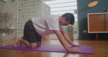 Young man practicing yoga on a mat in living room home interior. Person stretching body