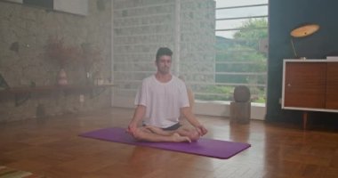 Young man meditating on mat in his living room at home.