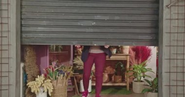 One female business woman sliding shutter door owner of flower store. Businesswoman of local shop opening store at sidewalk