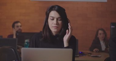 Latin kökenli genç bir bayan çalışan kulaklık takıyor bilgisayarın önünde, şirket çağrı merkezinde gece yarısı oturuyor. Genç kadın çağrı merkezi operatörü