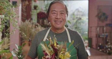 Florist business owner of flower store smiling at camera portrait face closeup holding plant