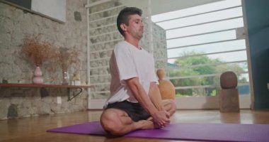 Man stretches on a mat in the living room and practices yoga. He does flexibility exercises and keeps himself fit and healthy.