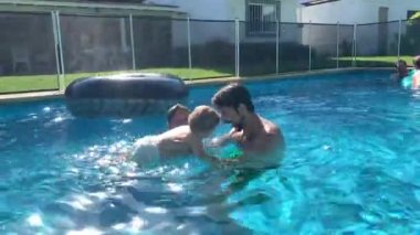 Babayla bebek havuzda kaynaşıyor. Baba küçük oğlunu havuzda tutuyor.