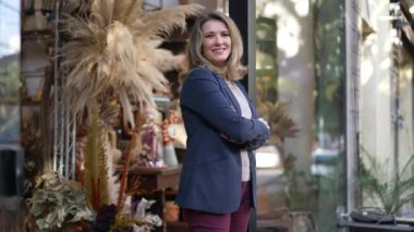 Middle age entrepreneur smiling standing in the door of her flower shop proud to be the owner of a small business standing by street sidewalk