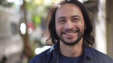 Portrait of a happy hispanic man walking forward in street. Smiling South American Brazilian person walks outdoors in urban environment in sunlight