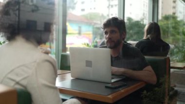 Kahve dükkanındaki insanlar camdan içeri giriyorlar. Kadın ve erkek müşteriler kafe restoranında konuşuyor. Dizüstü bilgisayarın önünde bayan arkadaşıyla sohbet eden kişi.