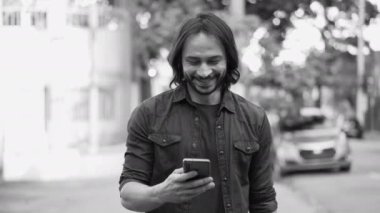 Happy young man looking at cellphone device walking in city street in monochromatic