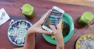 Yeşil meyve suları ve tabakta salata, kız akıllı telefonuyla fotoğraf çekiyor..
