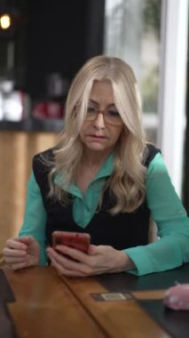 Üst düzey yönetici kadın kahve dükkanında akıllı telefon kullanıyor. Dikey Video 'daki kafeterya restoranında internet üzerinde gezinen kararsız yaşlı kişi