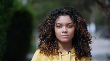Kendine güvenen siyah Latin bir kız kameraya doğru yürüyor. 20 'li yaşlardaki kıvırcık saçlı Afro-Amerikan kadın sokaklarda yürüyor.