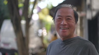 Portrait of a happy senior Asian man smiling at camera standing in city street. Closeup older joyful person face