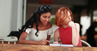 İki güzel çok ırklı arkadaş oturmuş menüye bakıyor ve konuşuyorlar.