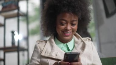 Mutlu Afro-Amerikan kadın cep telefonu kullanarak olumlu mesaj okuyor. Afro saçlı, gülümseyen siyah bir kız.