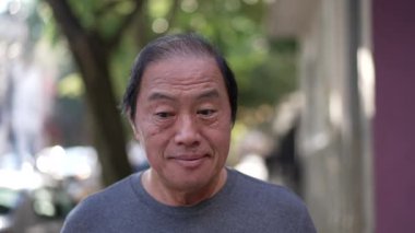 One pensive senior man having an idea breakthrough while walking outdoors. Portrait of a contemplative older middle aged Asian person in contemplation