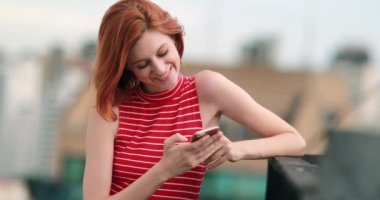 Kızıl saçlı genç kadın elinde akıllı telefon tutarken, aşık olurken, mesaj atarken mutlu hissediyor.