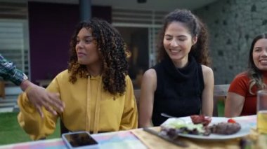 Neşe dolu bir grup arkadaş ve aile, öğle yemeği barbeküsünde ev partisinde konuşuyor.