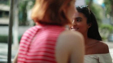 Sokak kaldırımında konuşan çok ırklı mutlu arkadaşlar. Genç kadınlar gülüyor ve gülümsüyor