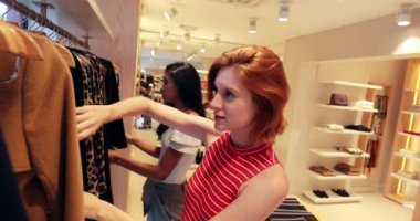 Genç kızıl saçlı kadın kıyafet alışverişi yapıyor, kız ne alacağını seçiyor..