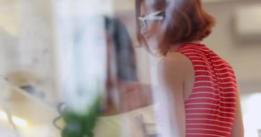 Güneş arayan genç kadın alışverişçiler mağazada ürün giyerler, güneş gözlüğü takan bir kızın penceresinden görülürler.