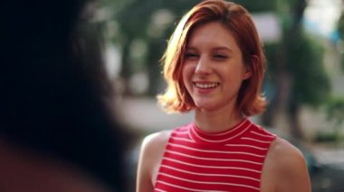 İki bayan arkadaş dışarıda güneş ışığında birbirleriyle konuşuyorlar. Kız arkadaşlar şehir güneşinin altında sohbet ediyorlar.