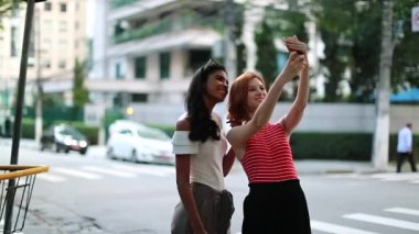 İki çok ırklı kız arkadaş dışarıda selfie çekiyor.