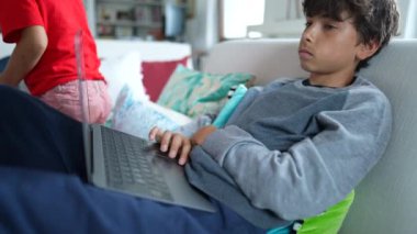 Kanepede oturan dizüstü bilgisayarda internette gezinen çocuk.