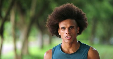 Happy confident young black african man walking forward at park feeling enthusiastic smiling and laughing