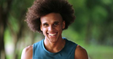 Happy confident young black african man walking forward at park feeling enthusiastic smiling and laughing