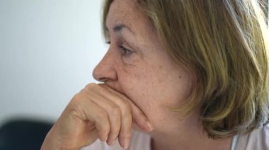 Konuşmaları dinleyen düşünceli yaşlı bir kadın.