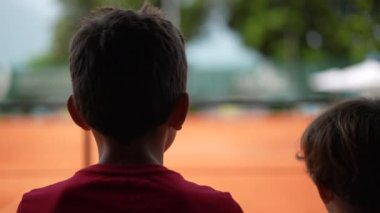 Tenis maçı izleyen çocuklar halka açık bir perspektiften maç izliyorlar. Çocuklar spor oyunu oynuyorlar