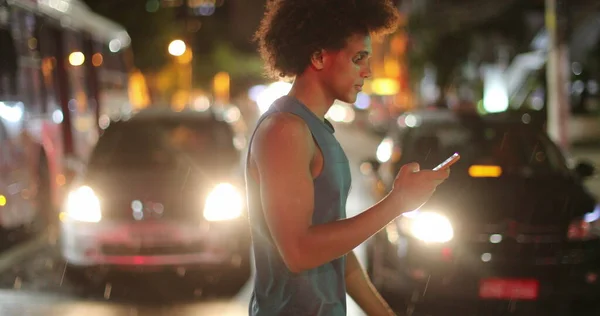 Young African Man Walking Night Looking Cellphone Device While Crossing — Stock Fotó