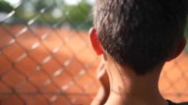 Tenis maçı çitlerine yaslanan çocuk spor maçı izliyor