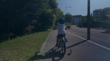 Bisiklet süren küçük çocuk kask takıyor.