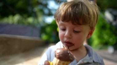 Küçük çocuk dışarıda çikolatalı dondurma yiyor.