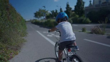 Bisiklet süren küçük çocuk kask takıyor.