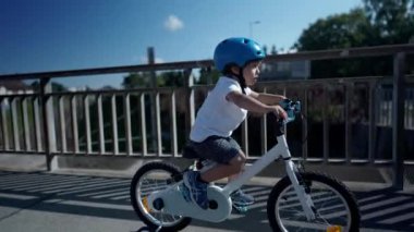 Çocuk dışarıda bisiklet sürüyor, koruyucu başlık takıyor.