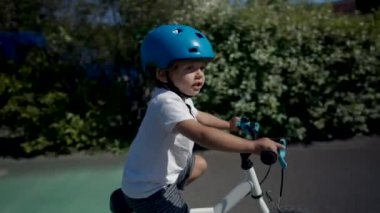 Aktif küçük çocuk dışarıda bisiklet sürüyor yeşil yolda kask takıyor.