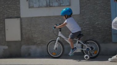 Sokak ortasında bisiklet süren çocuk kaldırımda bisiklet sürüyor.