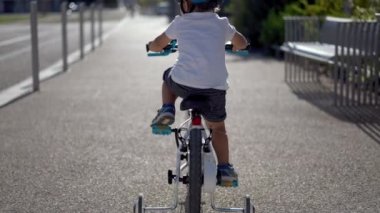 Dışarıda bisiklete binen küçük çocuğun arkasında.