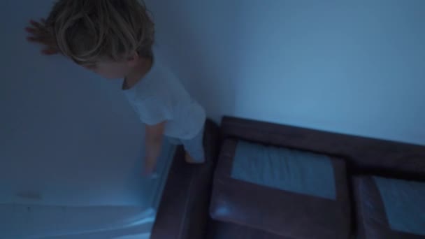 一个活泼的小男孩在家里的沙发上跑着 — 图库视频影像